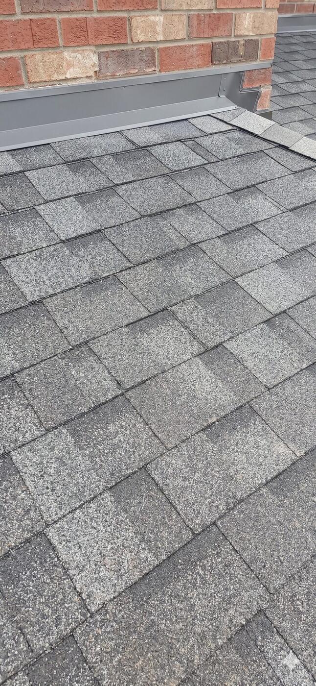 Close-up of asphalt shingles next to brick wall